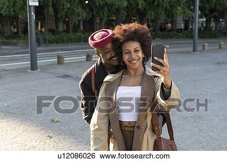 Stock Photograph - Couple taking selfie in street, Milan, Italy. Fotosearch