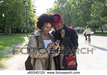 Stock Photography - Couple using cellphone in park, Milan, Italy. Fotosearch