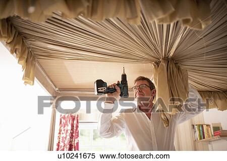 Stock Photography - Curtain fitter fitting canopy to four poster bed. Fotosearch