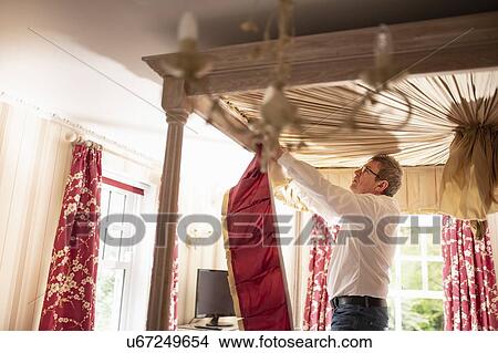 Picture - Curtain fitter fitting new pelmet to four poster bed. Fotosearch