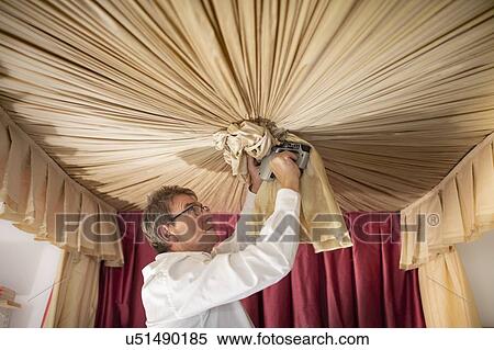 Stock Photography - Curtain fitter making 'Ruche' on canopy of four poster bed. Fotosearch