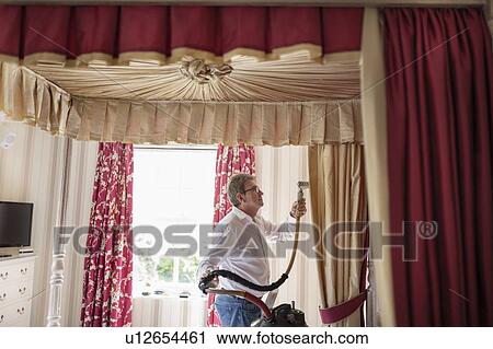 Stock Image - Curtain fitter using steam on material of four poster bed. Fotosearch