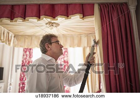 Stock Photograph - Curtain fitter using steam on material of four poster bed. Fotosearch
