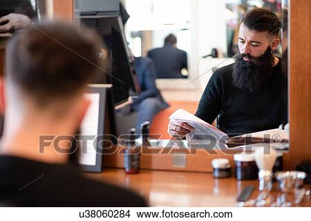 Picture - Customer waiting and reading in barber shop. Fotosearch