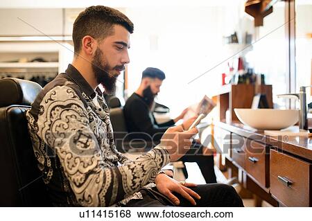 Stock Photo - Customers waiting and reading in barber shop. Fotosearch