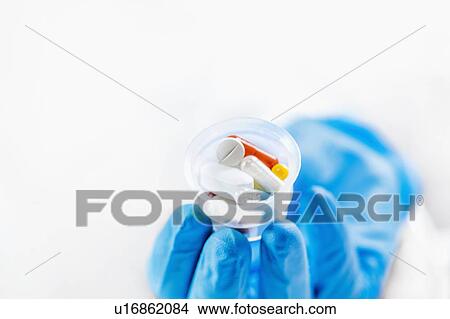 Doctor's hand in a glove holding graduated cup with pills View Large Photo Image Picture - Doctor's hand in a glove holding graduated cup with pills. Fotosearch