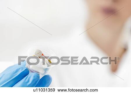 Stock Photo - Doctor's hand in a glove holding graduated cup with pills. Fotosearch