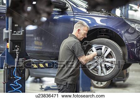 Stock Image - Engineer checking brakes in car service centre. Fotosearch