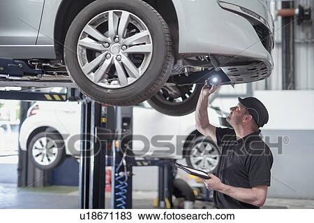 Stock Image - Engineer checking car on ramp in car service centre. Fotosearch