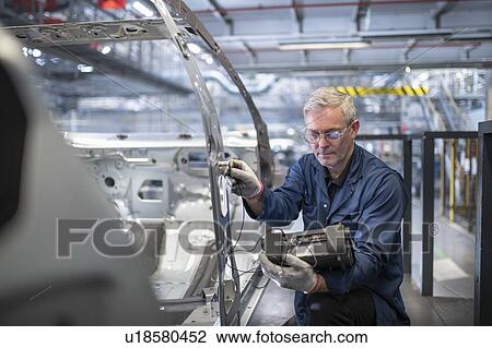 Stock Image - Engineer testing car body in car factory. Fotosearch