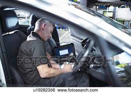 Stock Photograph - Engineer using computer to check car electronics in car service centre. Fotosearch