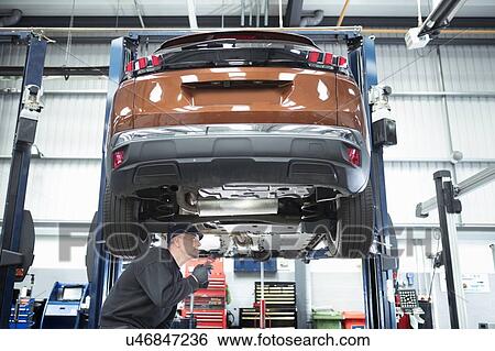 Stock Photograph - Engineer working under car on lift on car service centre. Fotosearch