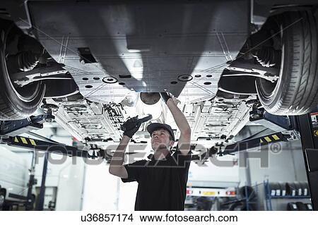 Picture - Engineer working underneath car on lift in car service centre. Fotosearch