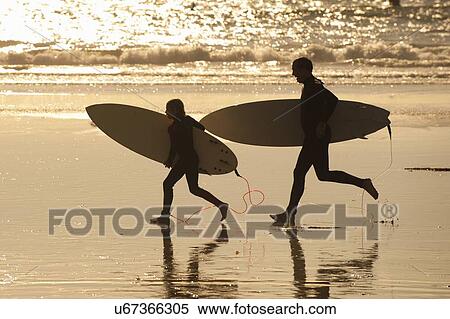 Stock Photography - Father and son carrying surfboards on beach at sunset. Fotosearch