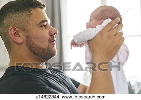 Picture - Father bonding with baby in arms at home. Fotosearch