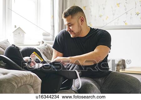 Picture - Father buckling up baby in baby cradle. Fotosearch