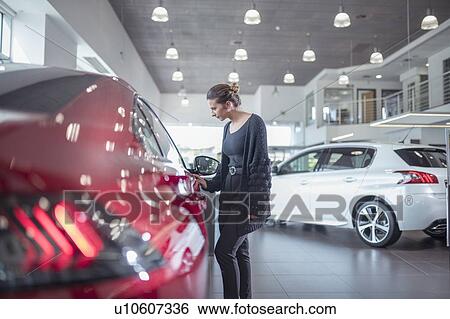 Stock Photograph - Female customer inspecting new car in car showroom. Fotosearch