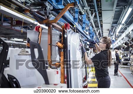 Stock Image - Female worker assembling car doors on production line in a car factory. Fotosearch