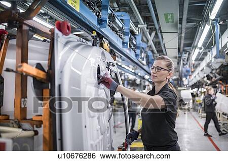 Stock Photograph - Female worker assembling car doors on production line in a car factory. Fotosearch