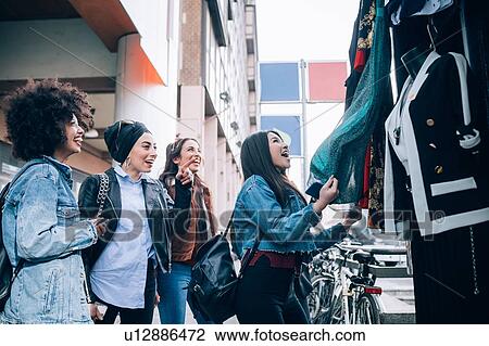 Stock Image - Friends admiring clothes in street stall, Milan, Italy. Fotosearch