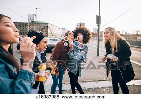 Stock Photo - Friends celebrating with confetti and soap bubbles in street, Milan, Italy. Fotosearch
