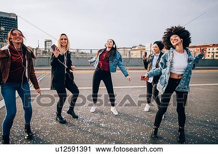 Stock Image - Friends dancing in street to smartphone music, Milan, Italy. Fotosearch