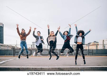 Stock Image - Friends jumping for joy in street, Milan, Italy. Fotosearch