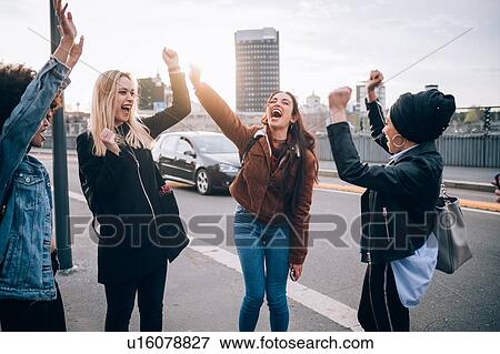 Stock Photo - Friends raising arms in triumph in street, Milan, Italy. Fotosearch