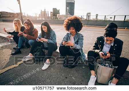Friends sitting on kerb texting, Milan, Italy View Large Photo Image Stock Photo - Friends sitting on kerb texting, Milan, Italy. Fotosearch