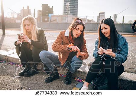 Friends sitting on kerb using smartphone, Milan, Italy View Large Photo Image Stock Photo - Friends sitting on kerb using smartphone, Milan, Italy. Fotosearch