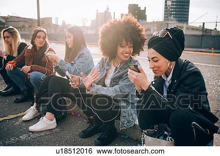Friends sitting on kerb using smartphone, Milan, Italy View Large Photo Image Stock Photograph - Friends sitting on kerb using smartphone, Milan, Italy. Fotosearch