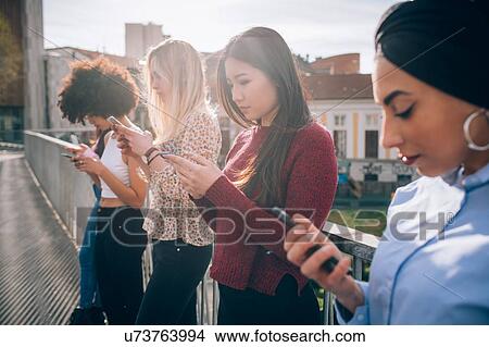 Picture - Friends standing by railing texting, Milan, Italy. Fotosearch