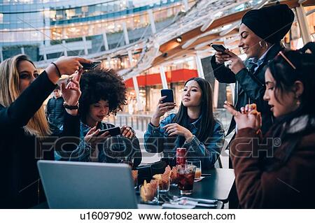Stock Image - Friends taking photos of their food and drinks at outdoor cafe, Milan, Italy. Fotosearch