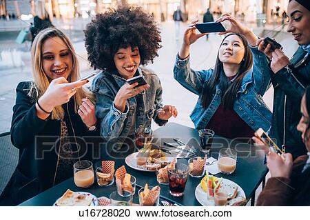 Friends taking photos of their food and drinks at outdoor cafe, Milan, Italy View Large Photo Image Stock Image - Friends taking photos of their food and drinks at outdoor cafe, Milan, Italy. Fotosearch