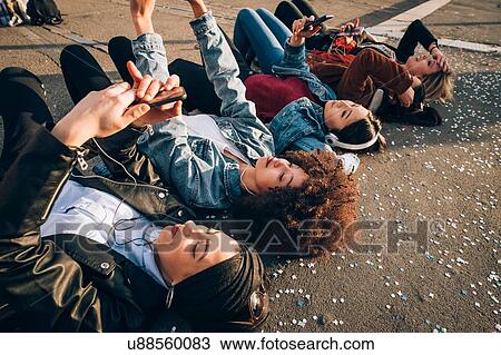 Stock Image - Friends together on kerb taking selfie and using smartphones, Milan, Italy. Fotosearch