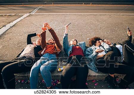 Stock Photography - Friends together on kerb taking selfie and using smartphones, Milan, Italy. Fotosearch