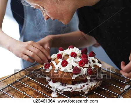 Girl and her sister baking a cake, decorating cake with fresh cream and raspberries at kitchen table, cropped View Large Photo Image Picture - Girl and her sister baking a cake, decorating cake with fresh cream and raspberries at kitchen table, cropped. Fotosearch