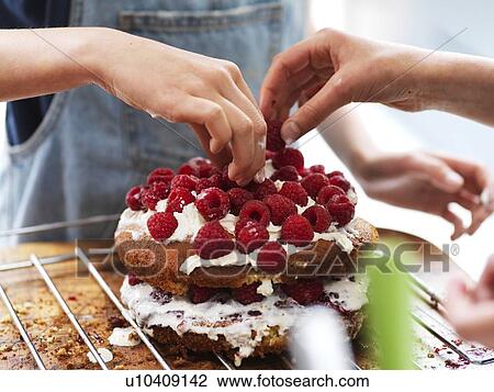 Girl and her sister baking a cake, decorating cake with fresh cream and raspberries at kitchen table, cropped view of hands View Large Photo Image Stock Image - Girl and her sister baking a cake, decorating cake with fresh cream and raspberries at kitchen table, cropped view of hands. Fotosearch