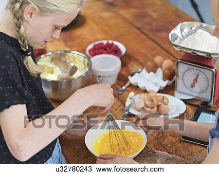 Girl and her sister baking a cake, whisking eggs in a bowl at kitchen table View Large Photo Image Stock Image - Girl and her sister baking a cake, whisking eggs in a bowl at kitchen table. Fotosearch