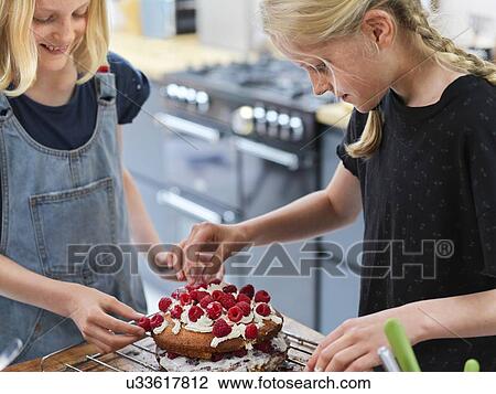Girl and her sister baking a cake, decorating cake with fresh cream and raspberries at kitchen table View Large Photo Image Stock Image - Girl and her sister baking a cake, decorating cake with fresh cream and raspberries at kitchen table. Fotosearch
