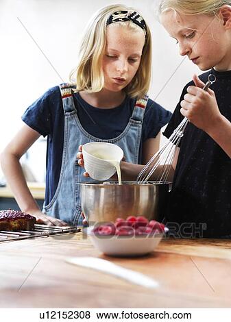 Girl and her sister baking a cake, pouring cream into mixing bowl at kitchen table View Large Photo Image Stock Photo - Girl and her sister baking a cake, pouring cream into mixing bowl at kitchen table. Fotosearch