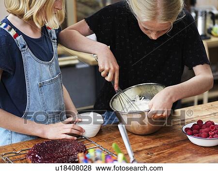 Stock Photo - Girl and her sister baking a cake, whisking cream in mixing bowl at kitchen table. Fotosearch