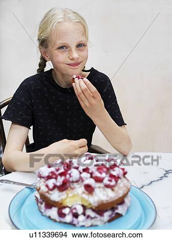 Girl eating her homemade cake with fresh raspberries at kitchen table, portrait View Large Photo Image Picture - Girl eating her homemade cake with fresh raspberries at kitchen table, portrait. Fotosearch