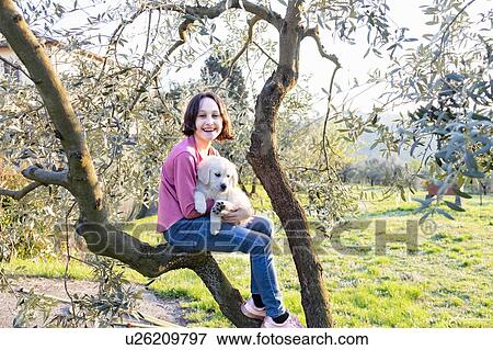 Stock Photo - Girl holding a cute golden retriever puppy on tree in orchard, portrait, Scandicci, Tuscany, Italy. Fotosearch
