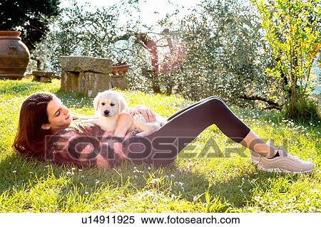 Stock Photography - Girl lying in orchard with a cute golden retriever puppy on her stomach, Scandicci, Tuscany, Italy. Fotosearch