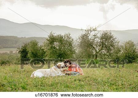 Stock Photograph - Girl sitting and petting labrador dog in scenic field landscape, Citta della Pieve, Umbria, Italy. Fotosearch