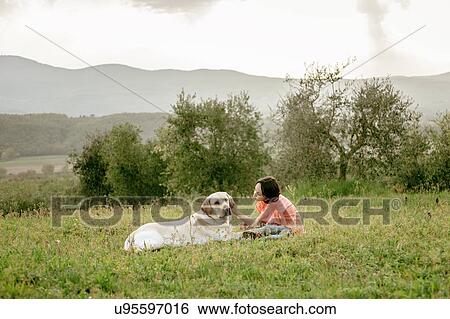 Stock Photograph - Girl sitting and petting labrador dog in scenic field landscape, Citta della Pieve, Umbria, Italy. Fotosearch