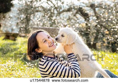 Stock Photo - Girl sitting in orchard playing with a cute golden retriever puppy, Scandicci, Tuscany, Italy. Fotosearch