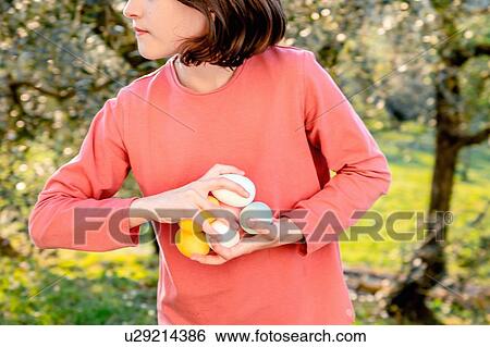 Stock Photograph - Girl with a handful of dyed Easter eggs in orchard, mid section, Scandicci, Tuscany, Italy. Fotosearch