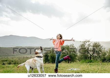 Stock Photo - Girl with open arms playing with labrador dog in scenic field landscape, Citta della Pieve, Umbria, Italy. Fotosearch